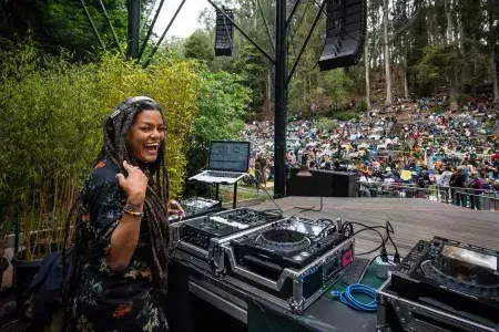 woman DJing at the Stern Grove Festival looks over her shoulder and smiles into the camera.